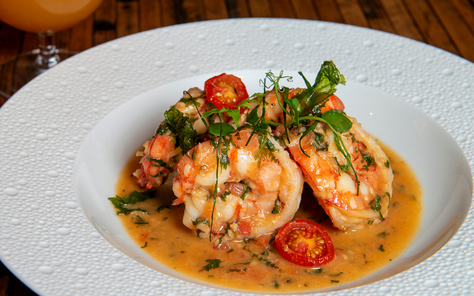 Shrimp and grits with cherry tomatoes and herbs in a white bowl.
