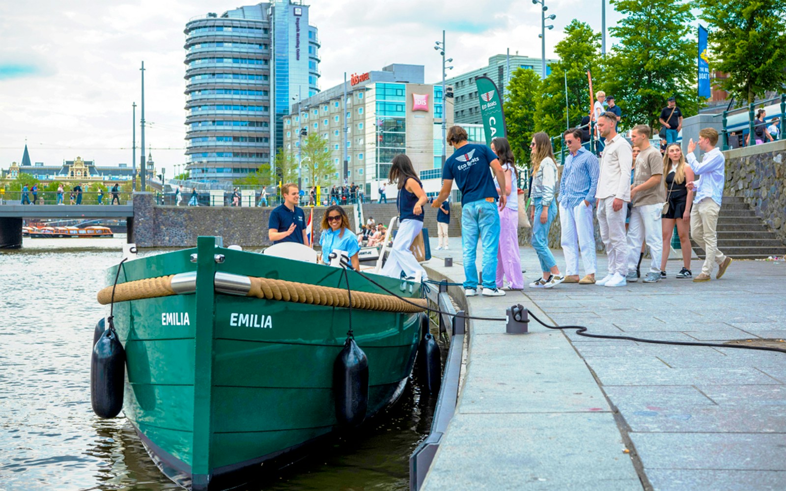 Amsterdam canal cruise boarding with passengers near modern buildings.