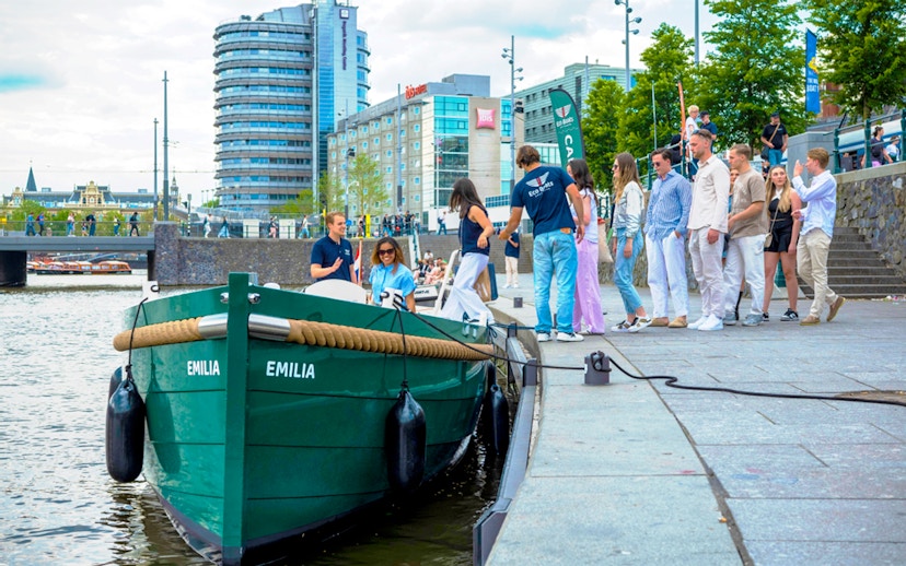 Amsterdam canal cruise boarding with passengers near modern buildings.