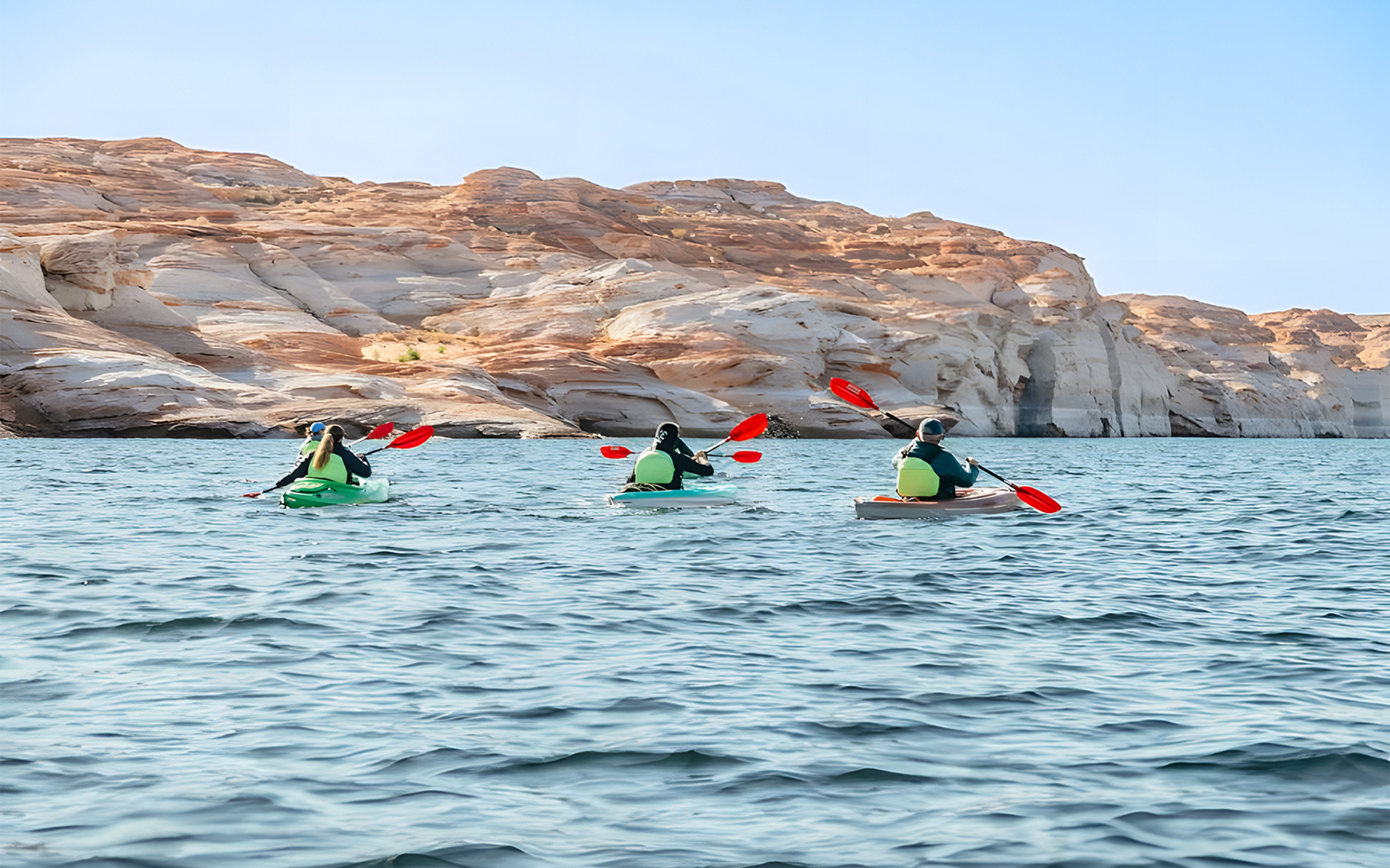 Kayakers paddling on Lake Powell near Antelope Canyon's sandstone cliffs.
