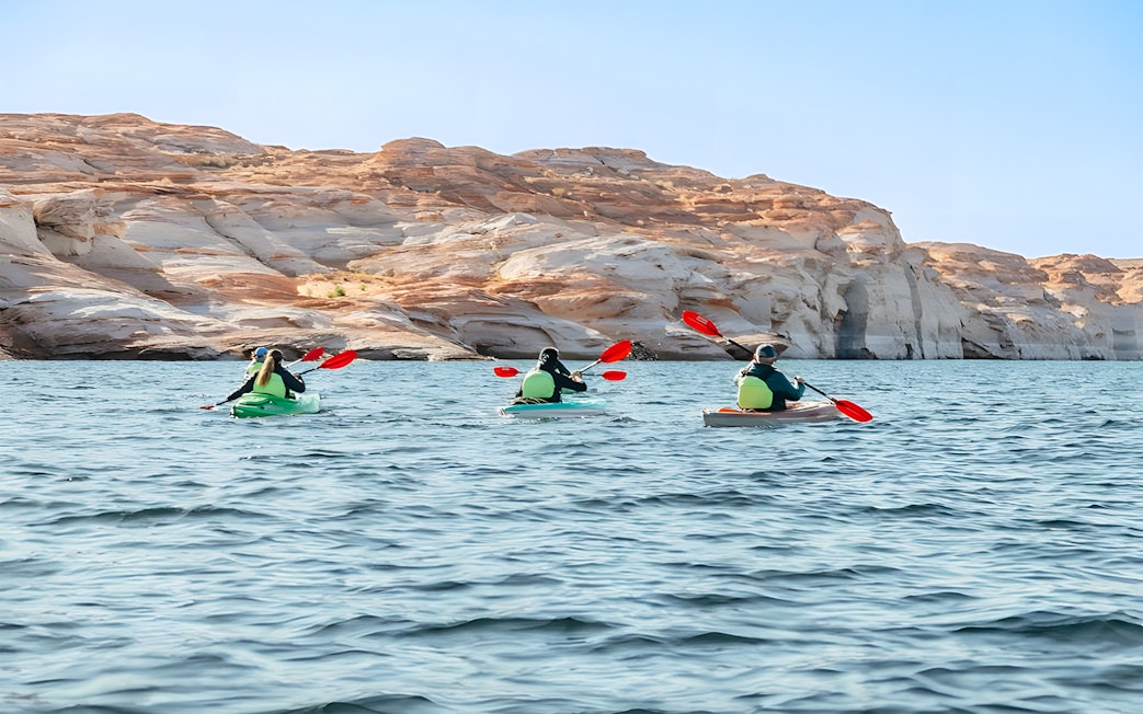 Kayakers paddling on Lake Powell near Antelope Canyon's sandstone cliffs.