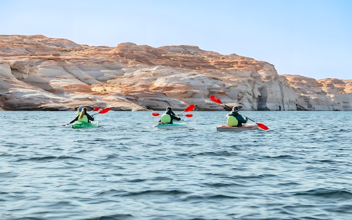 Kayakers paddling on Lake Powell near Antelope Canyon's sandstone cliffs.