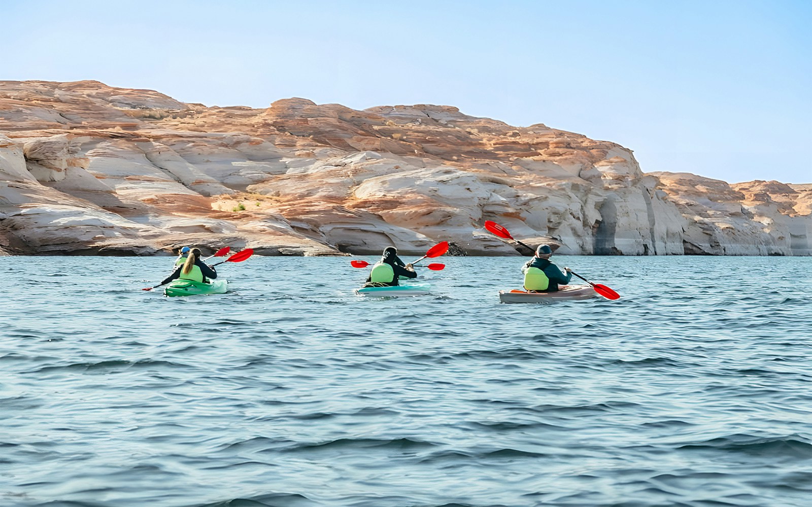 Kayakers paddling on Lake Powell near Antelope Canyon's sandstone cliffs.