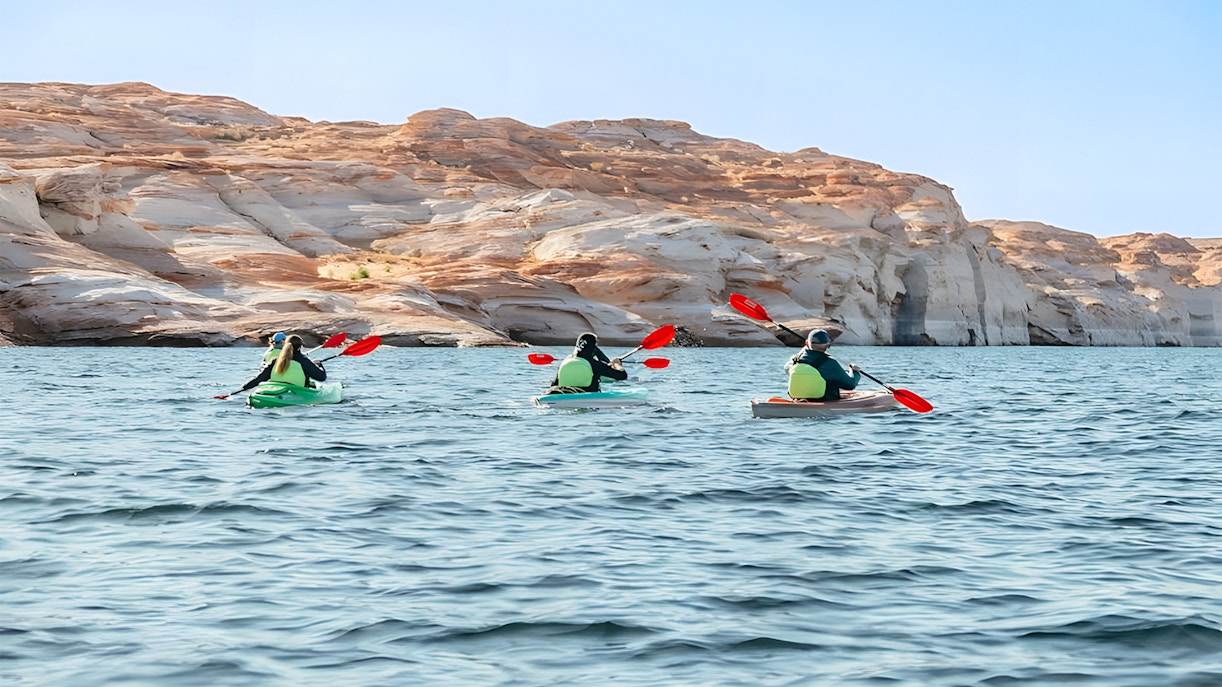 Kayakers paddling on Lake Powell near Antelope Canyon's sandstone cliffs.