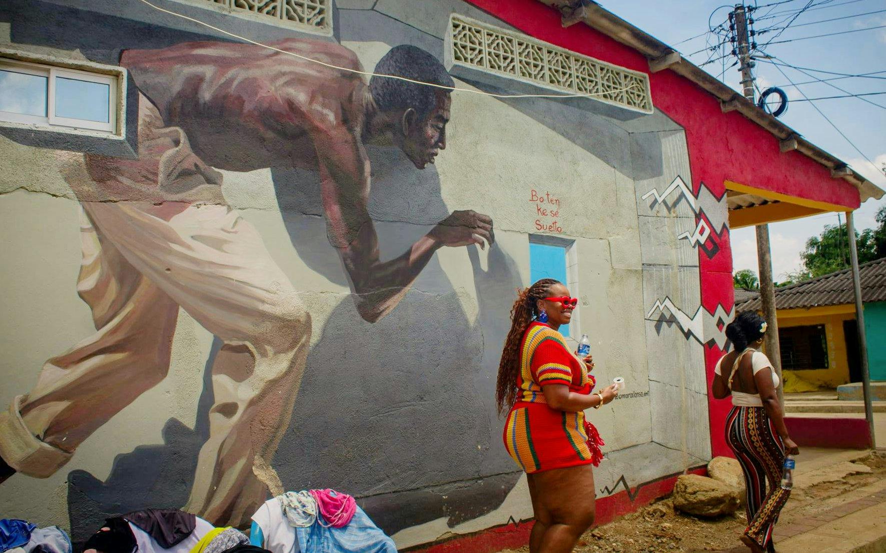 Street mural in San Basilio de Palenque depicting Afro-Colombian heritage with two women walking nearby.