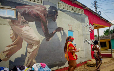 Street mural in San Basilio de Palenque depicting Afro-Colombian heritage with two women walking nearby.