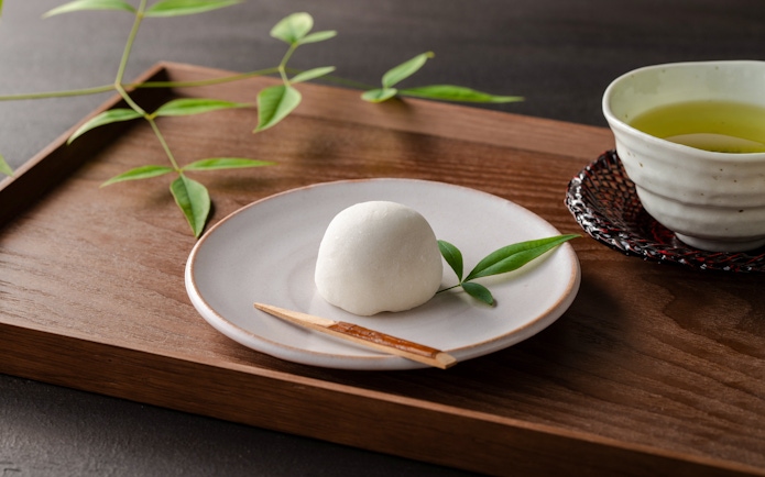 Wagashi sweet on a plate with matcha tea in a cup on a wooden tray.