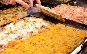 Assorted Italian pizzas being sliced in a bakery.