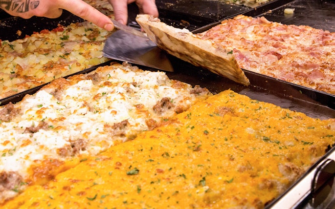 Assorted Italian pizzas being sliced in a bakery.