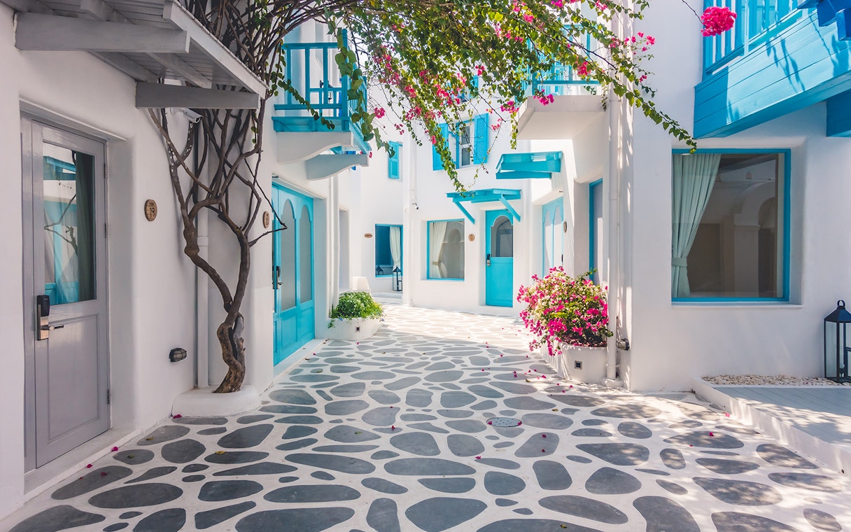 White-washed alley with blue accents and bougainvillea in Santorini, Greece.