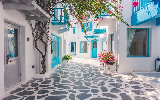 White-washed alley with blue accents and bougainvillea in Santorini, Greece.
