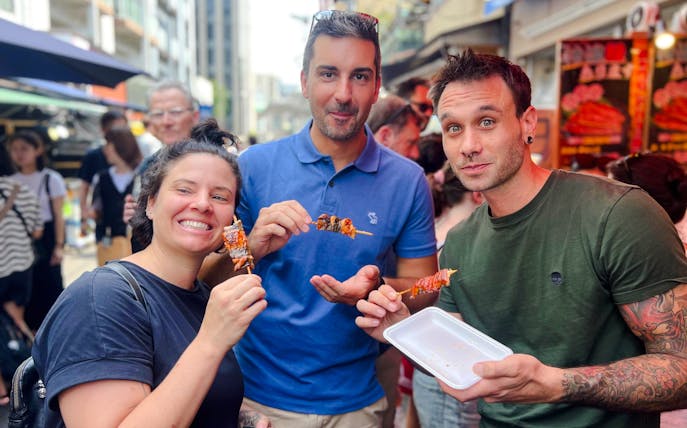 Tourists enjoying yakitori at Tsukiji Fish Market in Tokyo during a food tour.