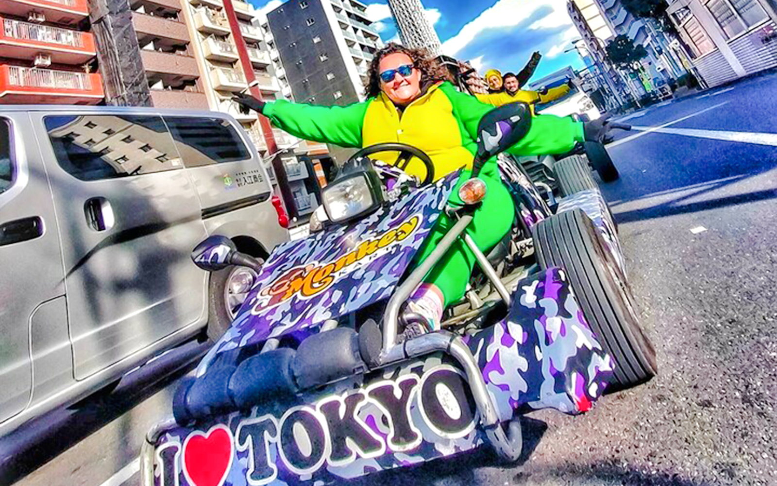 Woman in green costume driving a go-kart, giving peace sign in Tokyo street.