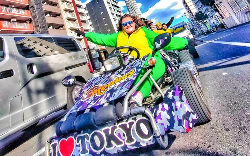 Woman in green costume driving a go-kart, giving peace sign in Tokyo street.