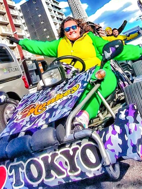 Woman in green costume driving a go-kart, giving peace sign in Tokyo street.