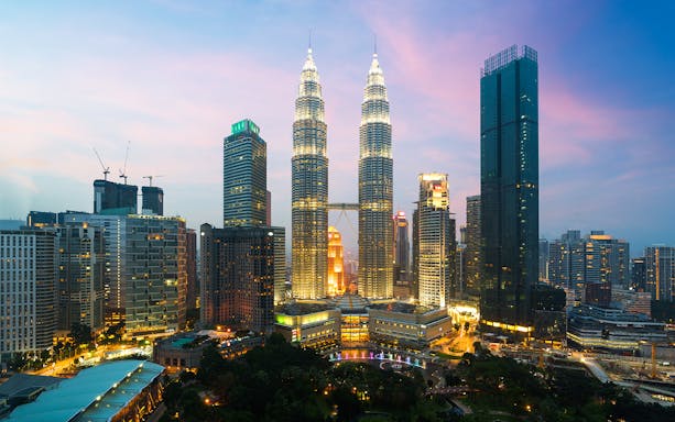 Petronas Twin Towers illuminated at dusk in Kuala Lumpur cityscape.
