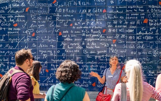 Tour guide explaining the Wall of Love in Montmartre, Paris, to a group of visitors.