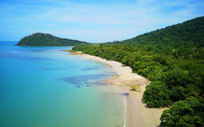 Cape Tribulation beach with lush rainforest and clear blue water, Australia.