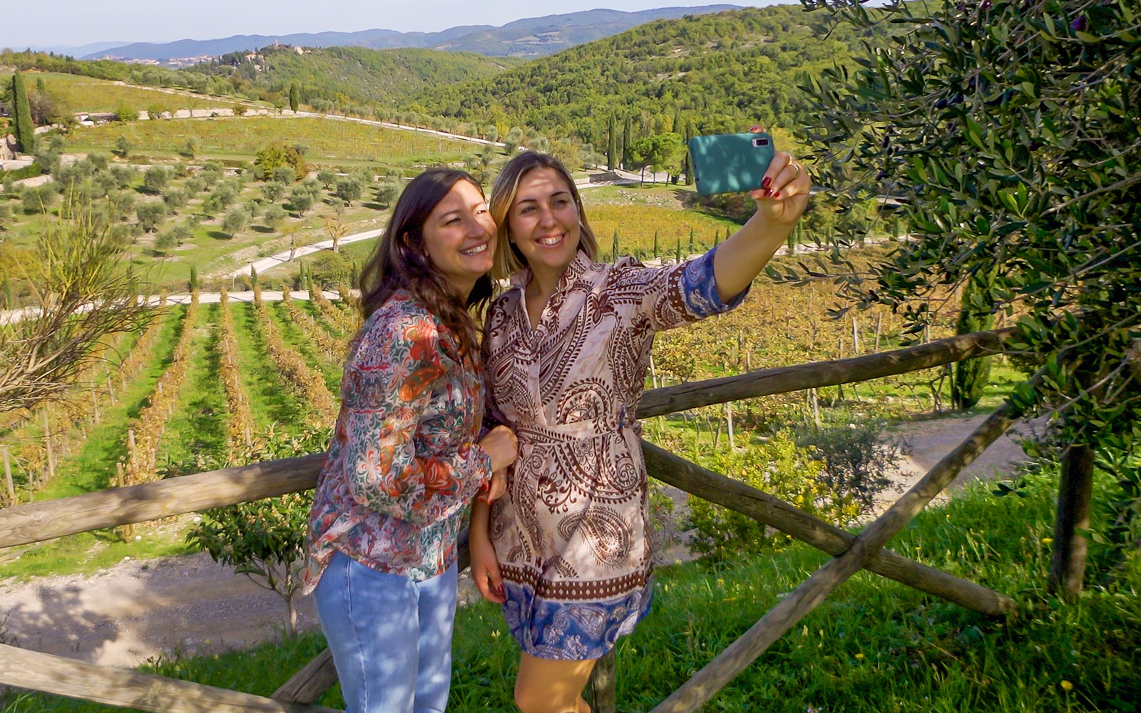 Visitors taking a selfie at a vineyard with scenic hills in the background.