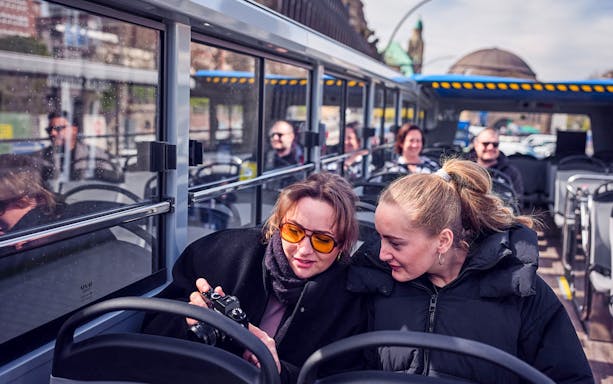 Passengers enjoying Hamburg hop-on hop-off bus tour, viewing camera photos.