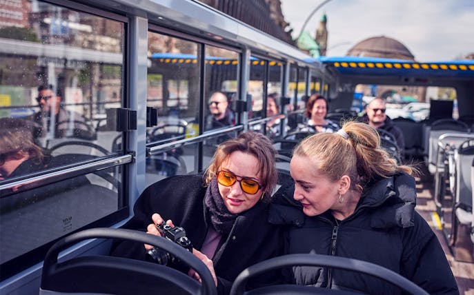 Passengers enjoying Hamburg hop-on hop-off bus tour, viewing camera photos.