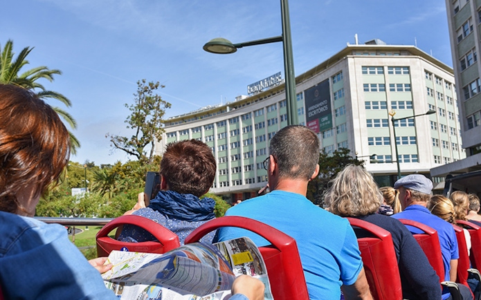 People on a hop-on hop-off bus tour in Lisbon, viewing city buildings.