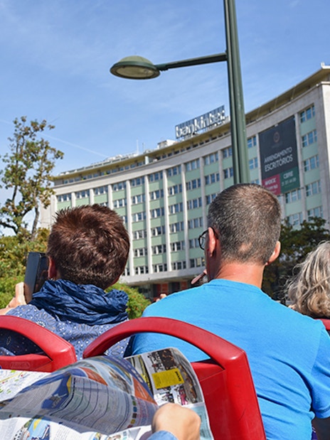 People on a hop-on hop-off bus tour in Lisbon, viewing city buildings.