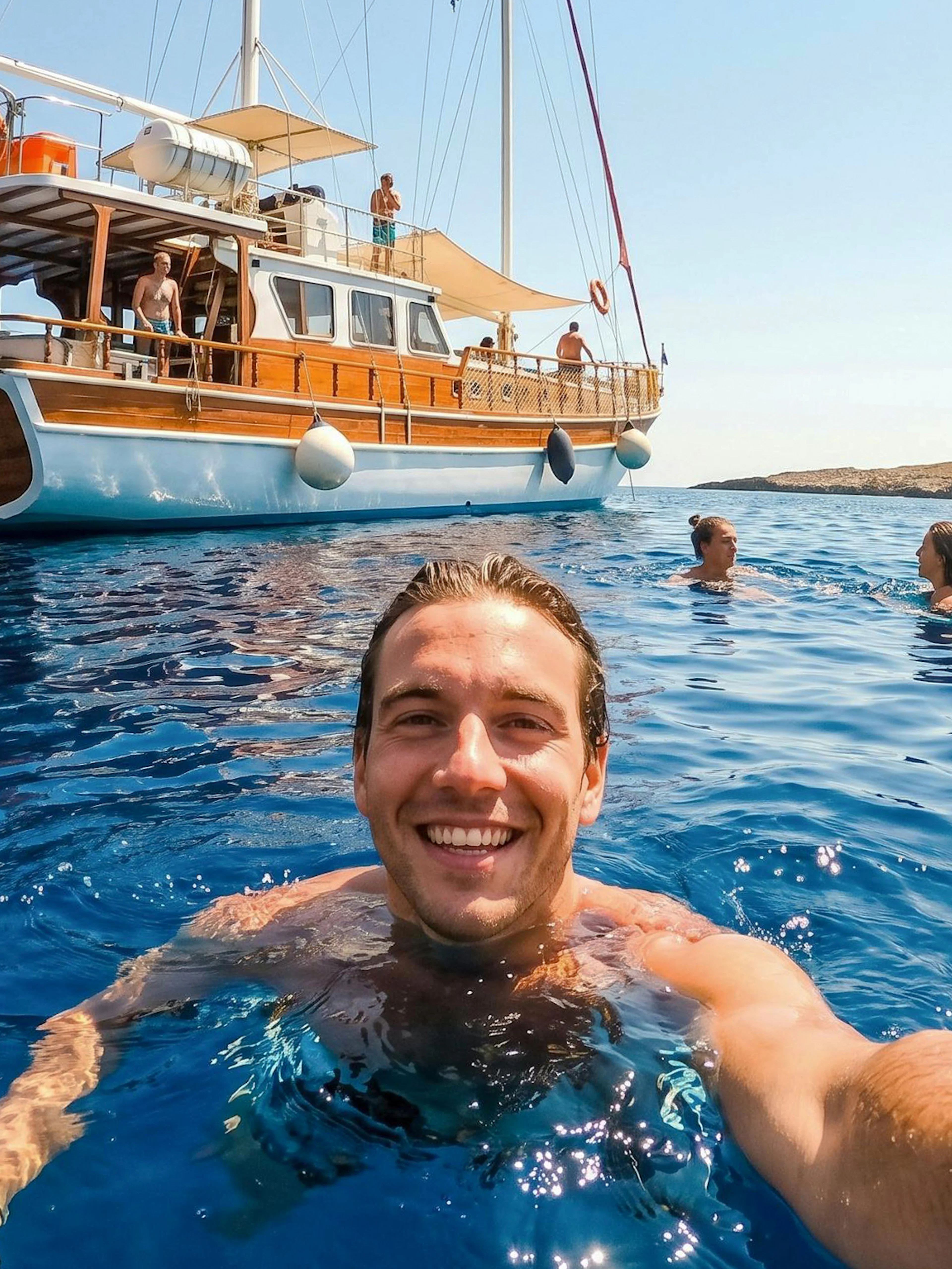 Sightseeing cruise in Rhodes with people swimming near a wooden boat.