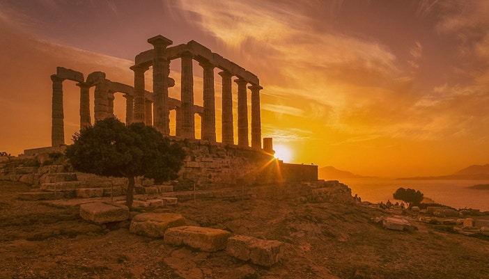 Temple of Poseidon at Cape Sounion silhouetted against a vibrant sunset sky.
