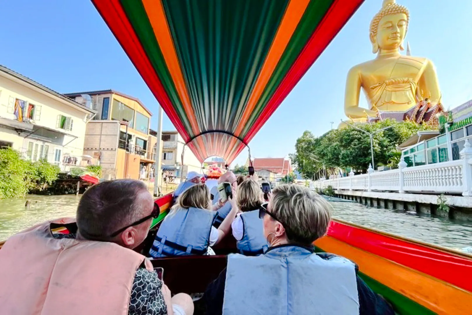 Tourists on a boat tour in Bangkok's canal, passing a large Buddha statue.
