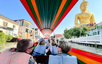 Tourists on a boat tour in Bangkok's canal, passing a large Buddha statue.