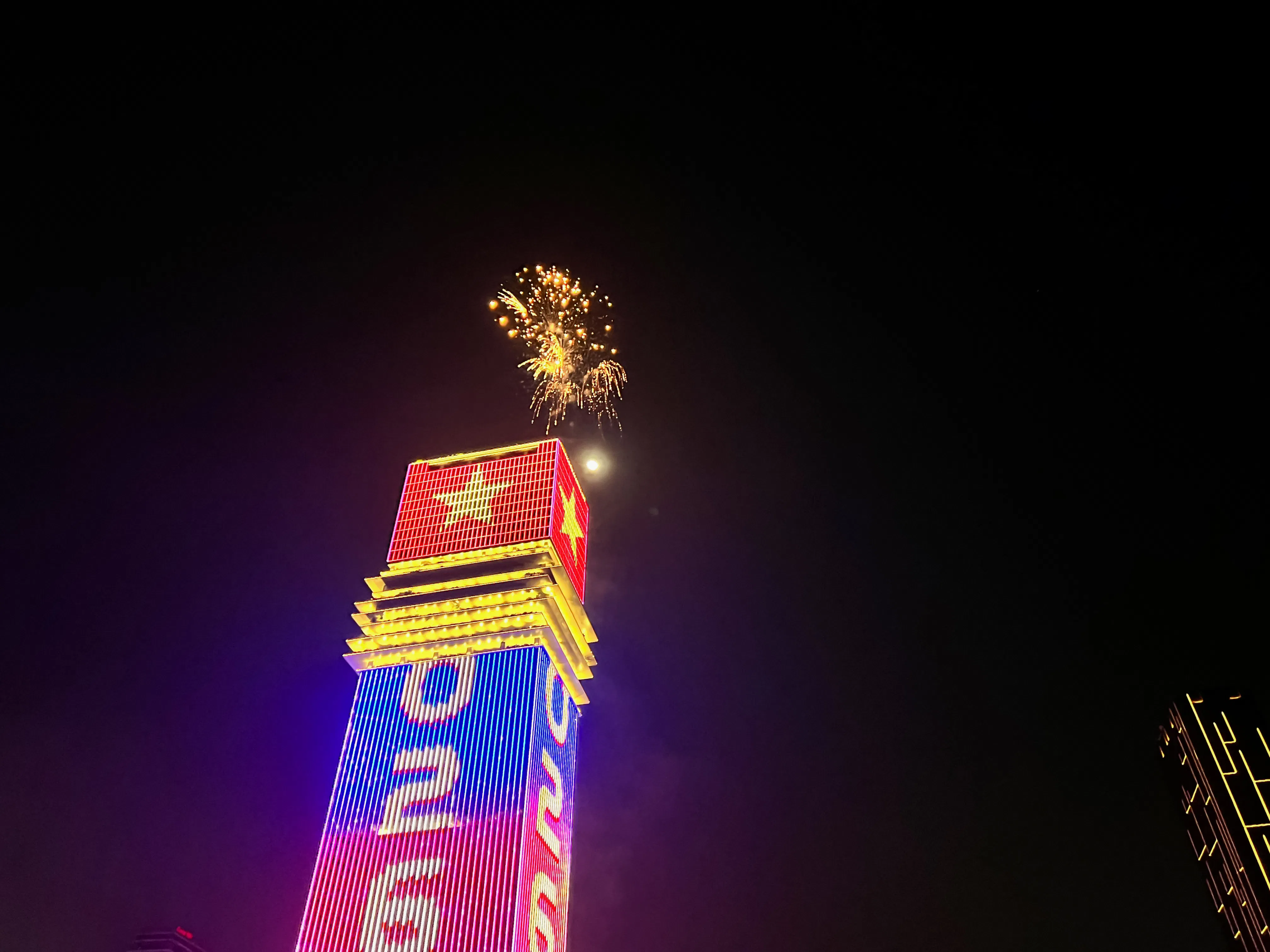 Fireworks above a lit skyscraper in Ho Chi Minh City during New Year’s Eve cruise.