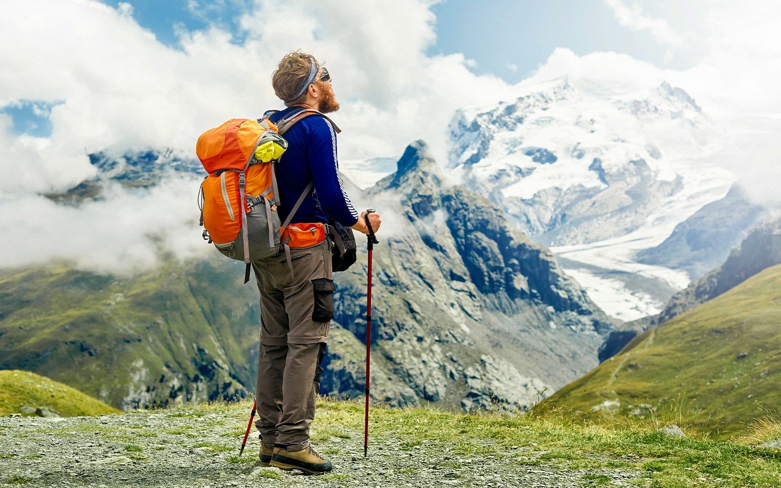 Hiker with backpack and poles overlooking snowy peaks at Klein Matterhorn, Switzerland.