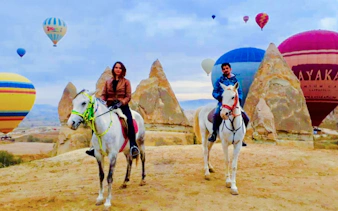 Guests on horseback with hot air balloons in Cappadocia at sunrise.