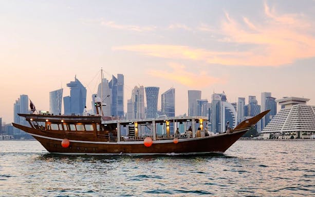 Qatari dhow boat cruising along Doha Corniche with city skyline in background.