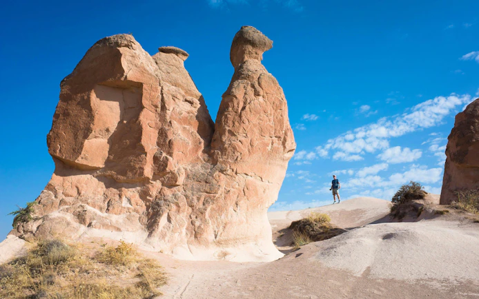 Rock formations in Cappadocia, Turkey with a person hiking nearby under a clear blue sky.