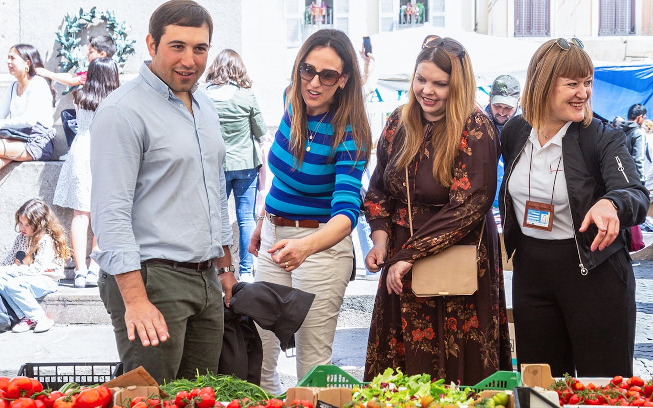 Tourists exploring fresh produce at Campo de' Fiori market during a guided street food tour.