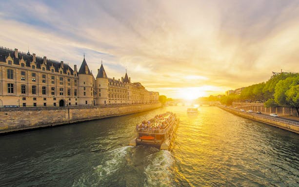 Bateaux Parisiens cruise on the Seine passing the Conciergerie in Paris, France at sunset.