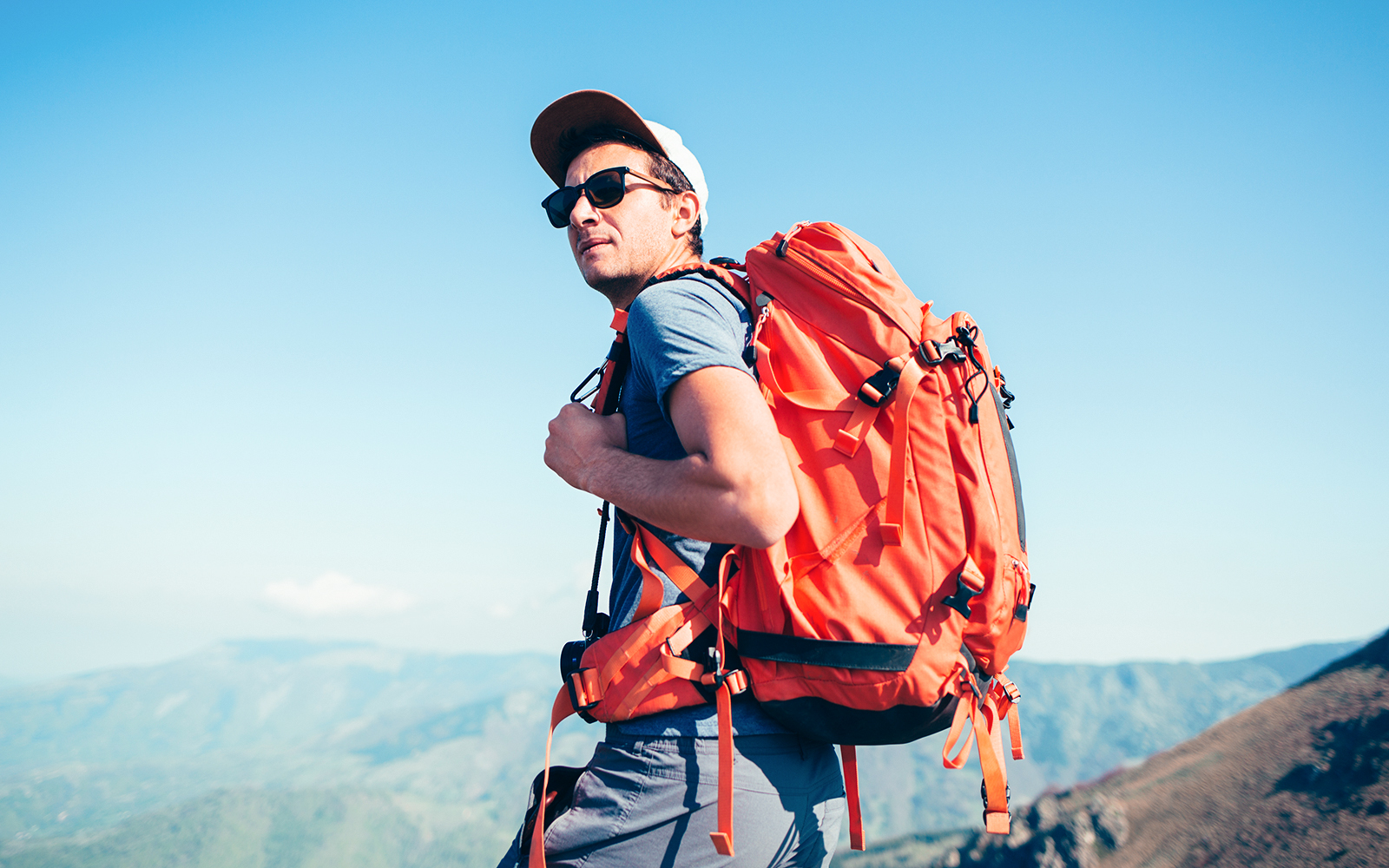 Backpacker with orange backpack hiking in mountainous landscape.