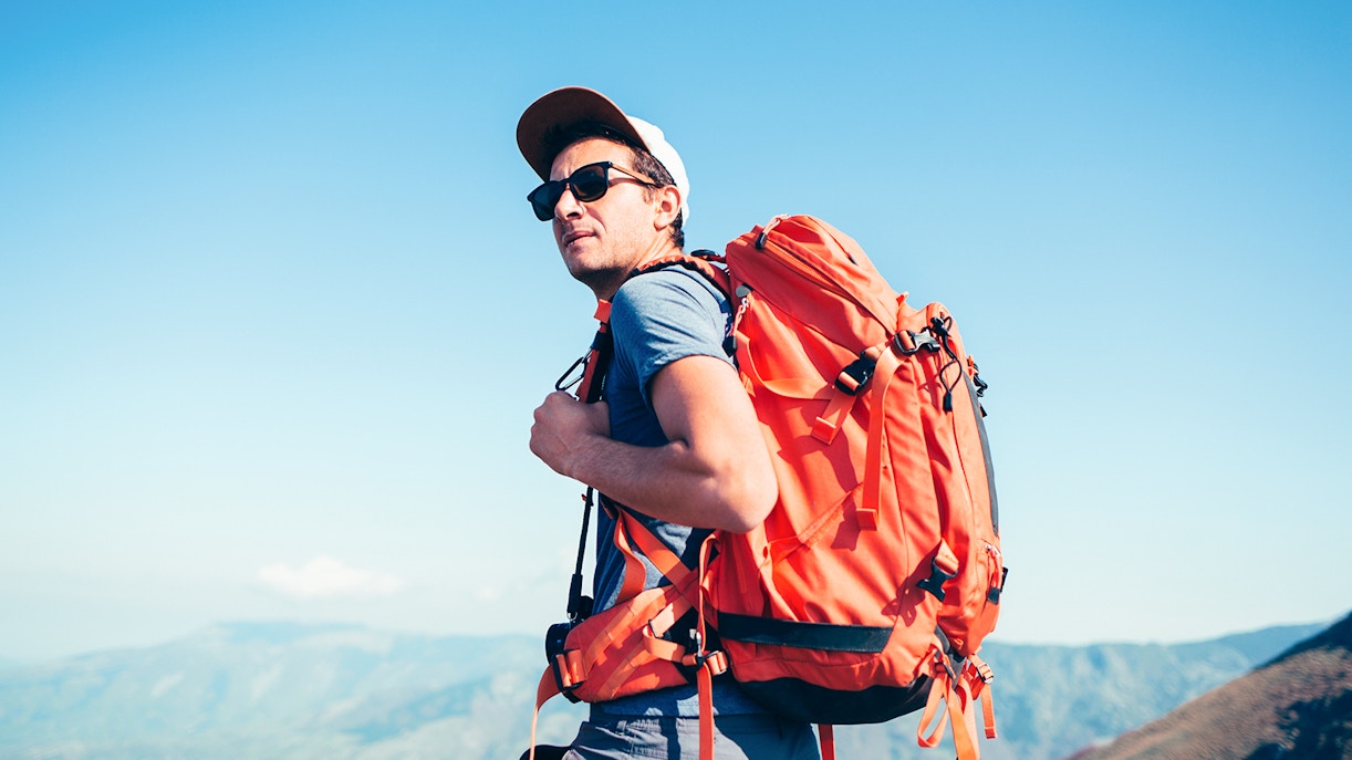 Backpacker with orange backpack hiking in mountainous landscape.