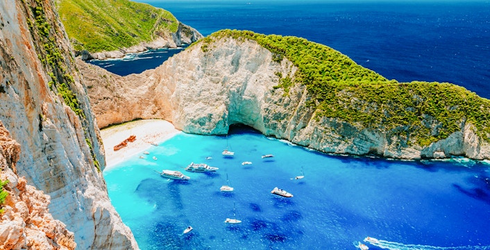 Navagio Beach on Zakynthos with shipwreck, turquoise water, and tourists on the sand.
