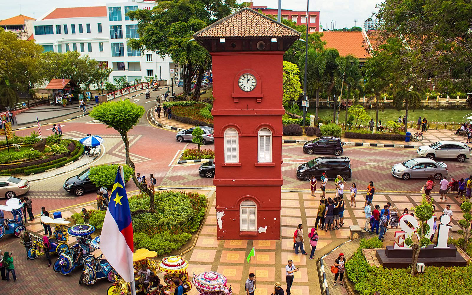 Old Town Hall Stadthuys on Red Square in Melaka with tourists and colorful trishaws.