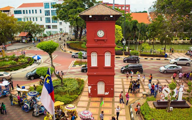 Old Town Hall Stadthuys on Red Square in Melaka with tourists and colorful trishaws.