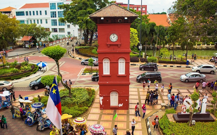 Old Town Hall Stadthuys on Red Square in Melaka with tourists and colorful trishaws.