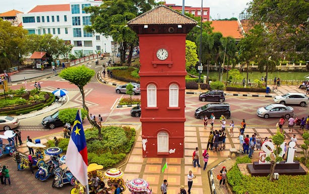 Old Town Hall Stadthuys on Red Square in Melaka with tourists and colorful trishaws.