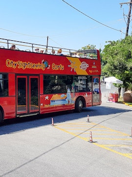 Red double-decker bus for City Sightseeing Corfu tour with passengers on top deck.