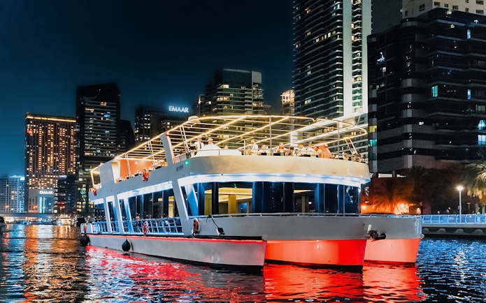 Sunset cruise boat with diners in Dubai Marina, skyscrapers illuminated in the background.