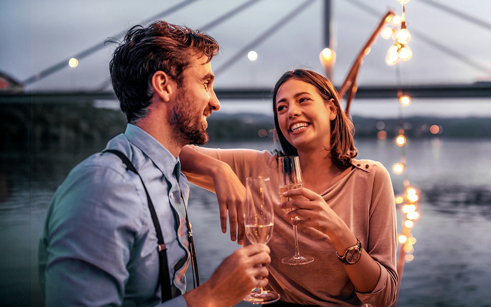 Couple enjoying champagne on an evening cruise in Düsseldorf with bridge lights in the background.