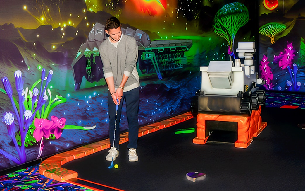 Blacklight mini golf course with guest putting near neon space-themed decor.