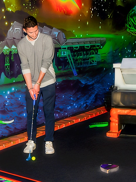 Blacklight mini golf course with guest putting near neon space-themed decor.